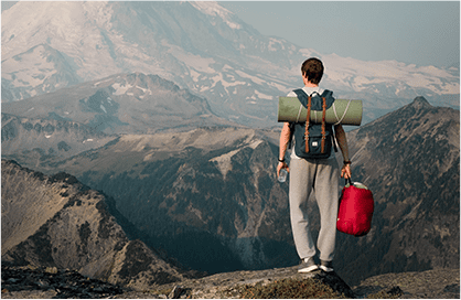 A man standing on top of a mountain holding a backpack.