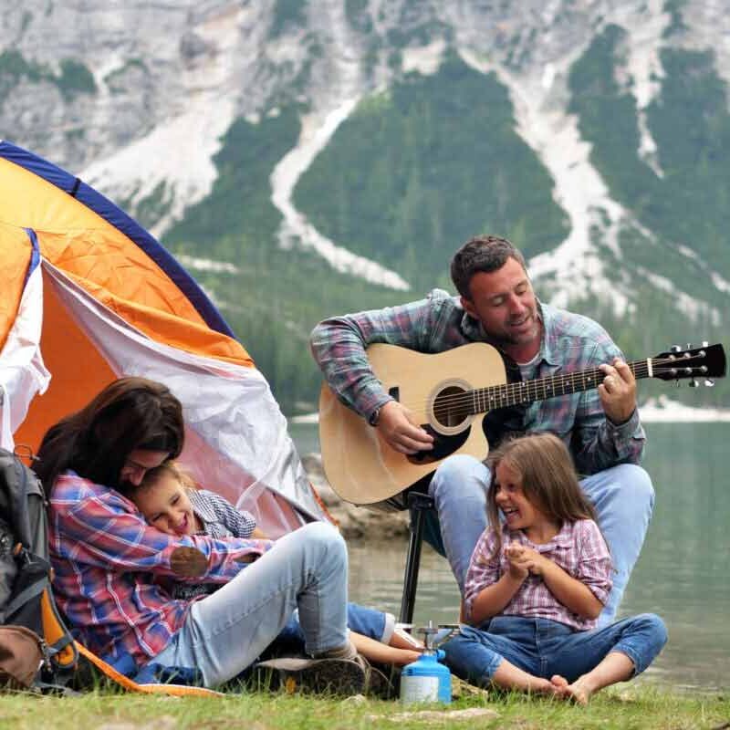 A family camping near the water with their guitar.